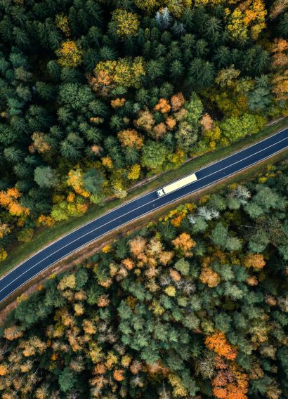 Arial view of heavy truck on a narrow twisting road. Autumn colorful trees by the sides of the road.